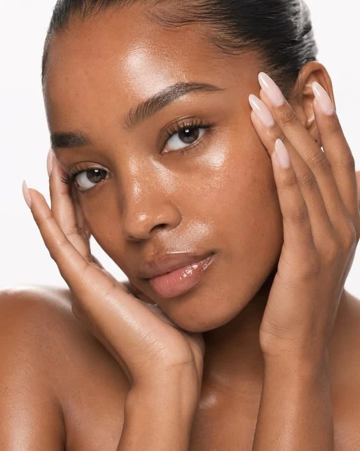 Femme aux mains posées sur le visage, peau lumineuse, fond blanc